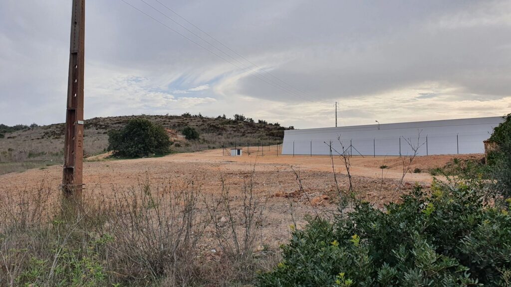 Modern industrial building with a white facade behind a fence in a dry landscape