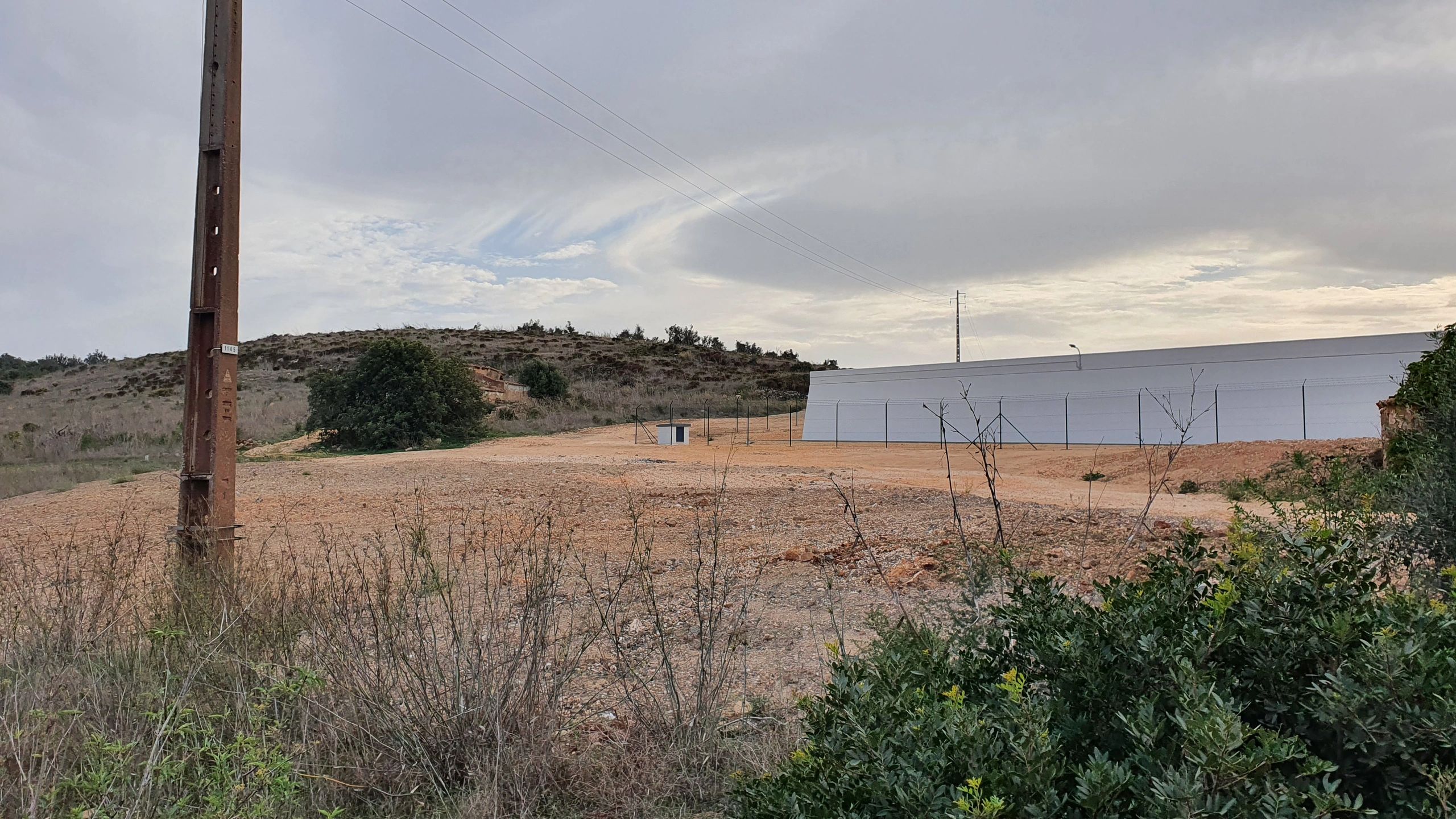 Modern industrial building with a white facade behind a fence in a dry landscape